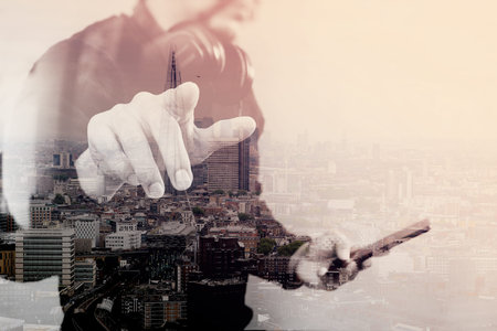 Double exposure of Businessman hand pressing an imaginary button,holding smart phone,blank digital screen graphic virtual,London architecture buildingsの写真素材