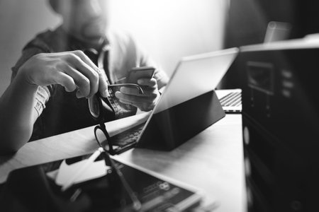Website designer holding eyeglasses and working digital tablet dock keyboard and computer laptop with smart phone and graphics design diagram and compact server on mable desk,black whiteの写真素材
