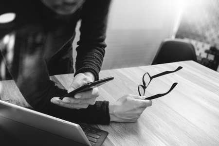 Businessman hand using mobile payments online shopping,omni channel,in modern office wooden desk,icons graphic interface screen,eyeglass,black whiteの写真素材