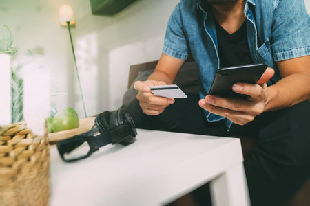 young man is sitting on a sofa shopping on line with smart phone is listening music with  headphones...