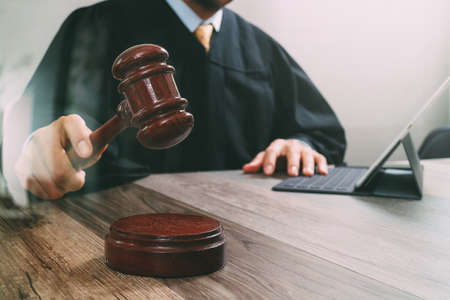 justice and law concept.Male judge in a courtroom striking the gavel,working with digital tablet computer docking keyboard on wood table,filter effectの写真素材