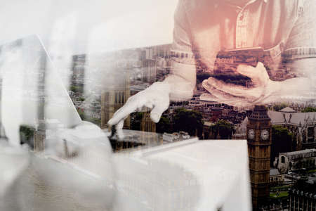 double exposure of designer man hand using laptop compter and mobile payments online shopping,omni channel,sitting on sofa in living room,green apples in wooden tray,London city buildingsの写真素材