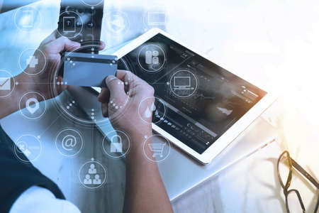 Designer Businessman hand using smart phone,mobile payments online shopping,omni channel,digital tablet docking keyboard computer in modern office on wooden desk,virtual interface icons screenの写真素材
