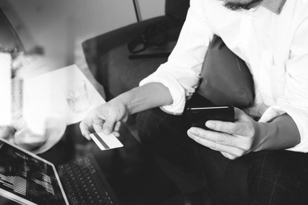 hipster hand using smart phone and laptop compter,holding cradit card payments online business,sitting on sofa in living room,green apples in wooden tray,black and whiteの写真素材