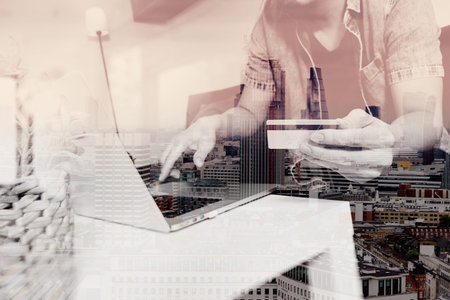 double exposure of hipster hand using laptop compter,holding cradit card payments online shopping or business,sitting on sofa in living room,green apples in wooden tray,London city buildingsの写真素材