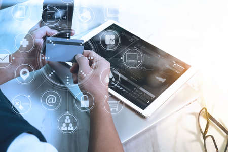 young man shopping on line with smart phone is listening music with headphones is holding a credit card on his hand at home,omni channel graphics interface screenの写真素材