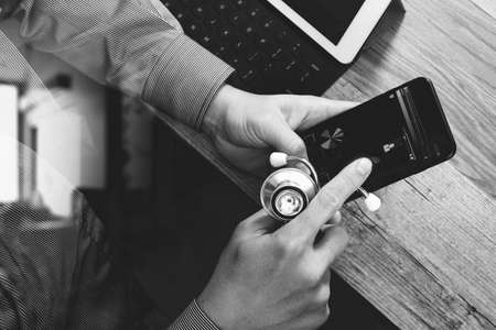 top view of medical doctor hand working with smart phone,digital tablet computer,stethoscope eyeglass,on wooden desk,black and whiteの写真素材