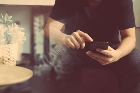 designer man hand using smart phon for mobile payments online shopping,omni channel,sitting on sofa in living room,vase rattan with plant and wooden tray on table,filterの写真素材