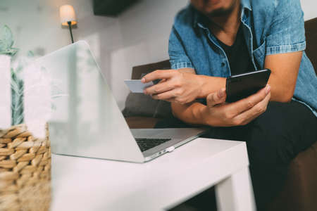 hipster hand using smart phone and laptop compter,holding cradit card payments online business,sitting on sofa in living room,green apples in wooden tray,filterの写真素材