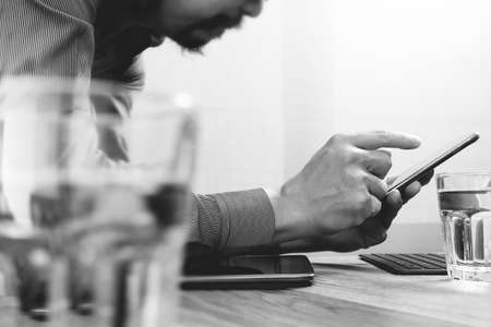 Businessman hand using mobile payments online shopping,omni channel,laptop computer on wooden desk,black whiteの写真素材
