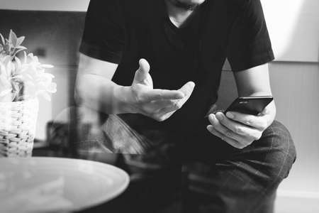 designer man hand using smart phon for mobile payments online shopping,omni channel,sitting on sofa in living room,vase rattan with plant and wooden tray on table,black and whiteの写真素材
