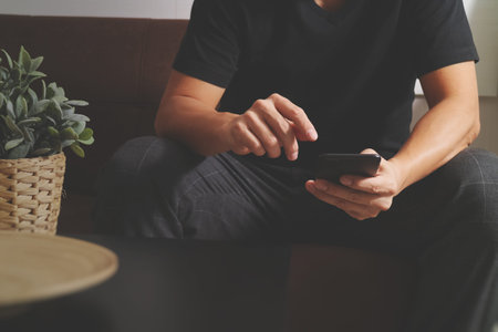 designer man hand using smart phon for mobile payments online shopping,omni channel,sitting on sofa in living room,vase rattan with plant and wooden tray on tableの写真素材