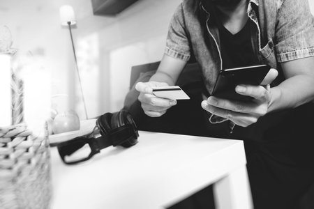 young man is sitting on a sofa shopping on line with smart phone is listening music with  headphones...