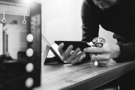 medical doctor hand working with smart phone,digital tablet computer,holding stethoscope,compact server on wood desk,black and whiteの写真素材