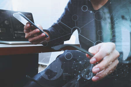 Designer hand using mobile payments online shopping,omni channel,laptop computer on wooden desk,digital screen graphic virtual icons,graph,diagramの写真素材