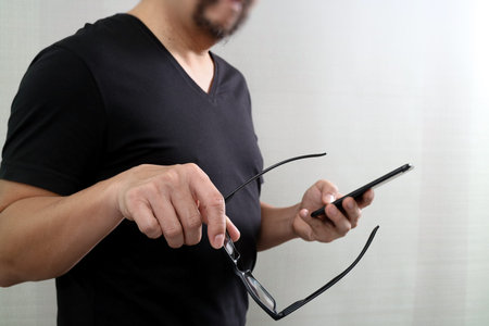 Designer hand holding eyeglasses,using smart phone on white background