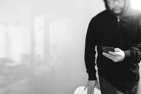 hipster male in a hood hand using mobile phone payments online shopping,omni channel,front view,black and whiteの写真素材