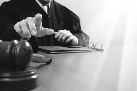 justice and law concept.Male judge in a courtroom with the gavel,working with smart phone,digital tablet computer docking keyboard,eyeglasses,on wood table,black and whiteの写真素材