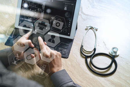 medical doctor hand working with smart phone,digital tablet computer,stethoscope eyeglass,on wooden desk,virtual graphic interface icons screenの写真素材