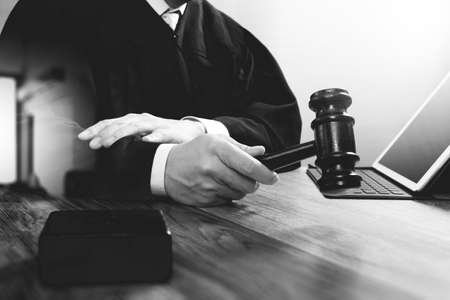 justice and law concept.Male judge in a courtroom with the gavel,working with digital tablet computer docking keyboard on wood table,black and whiteの写真素材