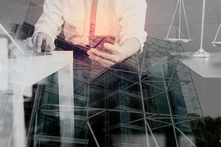 Double exposure of Justice and Law context.Male lawyer hand sitting on sofa and working with smart phone,digital tablet computer docking keyboard with gavel and document on living table at home,London architecture cityの写真素材