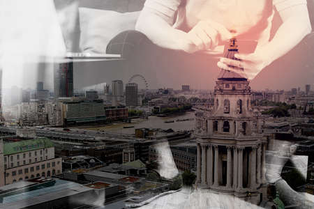 double exposure of hipster hand using digital tablet docking keyboard and smart phone for mobile payments online business,omni channel,sitting on sofa in living room,London architecture cityの写真素材