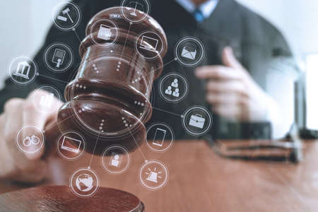 justice and law concept.Male judge in a courtroom with the gavel,working with smart phone,digital tablet computer docking keyboard,eyeglasses,on wood table,virtual interface graphic icons diagramの写真素材