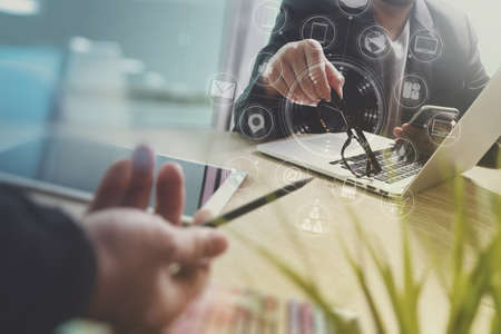 Designer Businessman hand using smart phone,mobile payments online shopping,omni channel,digital tablet docking keyboard computer in modern office on wooden desk,virtual interface icons screenの写真素材