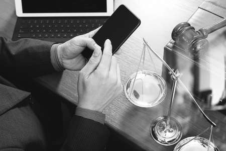 justice and law concept.Male lawyer in office with the gavel,working with smart phone,digital tablet computer docking keyboard,brass scale,on wood table,black and whiteの写真素材