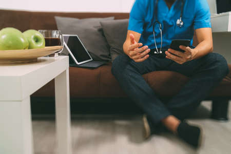 Medical and Health context,doctor hand working with smart phone,digital tablet computer,stethoscope,sitting on sofa in living room,filterの写真素材