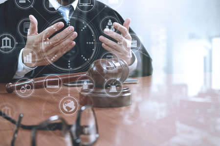 justice and law concept.Male judge in a courtroom with the gavel,working with smart phone,digital tablet computer docking keyboard,eyeglasses,on wood table,virtual interface graphic icons diagramの写真素材