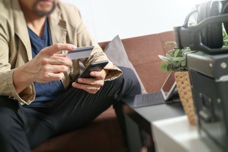 hipster hand using smart phone,digital tablet docking keyboard,holding cradit card payments online business,sitting on sofa in living room,work at home conceptの写真素材