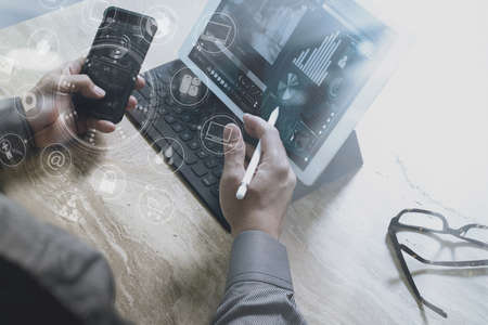 Designer Businessman hand using smart phone,mobile payments online shopping,omni channel,digital tablet docking keyboard computer in modern office on wooden desk,virtual interface icons screenの写真素材