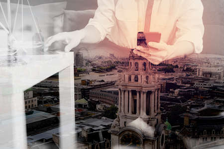 Double exposure of Justice and Law context.Male lawyer hand sitting on sofa and working with smart phone,digital tablet computer docking keyboard with gavel and document on living table at home,London architecture cityの写真素材