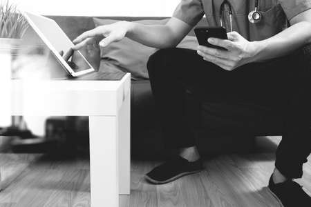 Medical and Health context,doctor hand working with smart phone,digital tablet computer,stethoscope,sitting on sofa in living room,black and whiteの写真素材