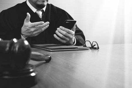 justice and law concept.Male judge in a courtroom with the gavel,working with smart phone,digital tablet computer docking keyboard on wood table,black and whiteの写真素材