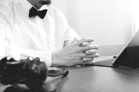 Justice and Law context.Male lawyer hand working with smart phone,digital tablet computer docking keyboard with gavel and document on wood table,black and whiteの写真素材