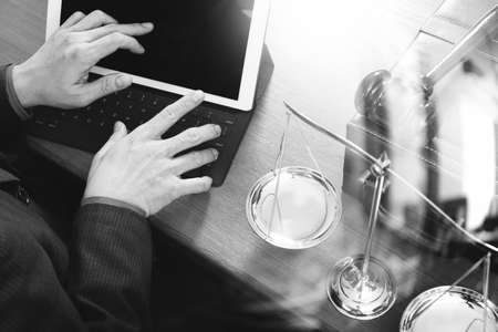 justice and law concept.Male lawyer in office with the gavel,working with smart phone,digital tablet computer docking keyboard,brass scale,on wood table,black and whiteの写真素材