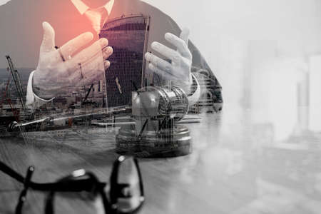 double exposure of justice and law concept.Male judge in a courtroom with the gavel,working with smart phone,digital tablet computer docking keyboard,on wood table,London architecture cityの写真素材