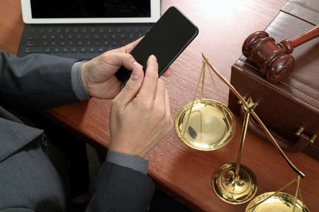 justice and law concept.Male lawyer in office with the gavel,working with smart phone,digital tablet computer docking keyboard,brass scale,on wood tableの写真素材