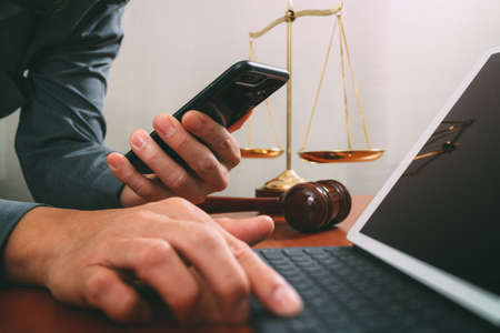 justice and law concept.Male lawyer in office with the gavel,working with smart phone and digital tablet computer and brass scale on wood tableの写真素材