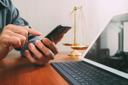 justice and law concept.Male lawyer in office with the balance brass scale,hand working with smart phone and digital tablet computer on wooden deskの写真素材