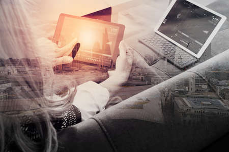 brunette woman using digital talet and laptop computer on sofa in living room with London city exposureの写真素材