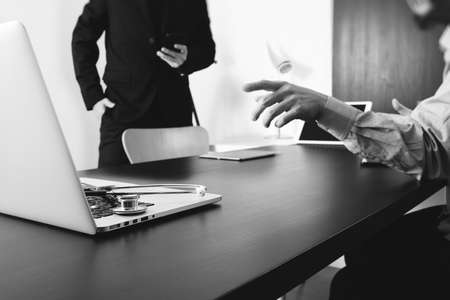 Medical co working concept,Doctor working with smart phone and digital tablet and laptop computer to meeting his team in modern office at hospital,black and whiteの写真素材