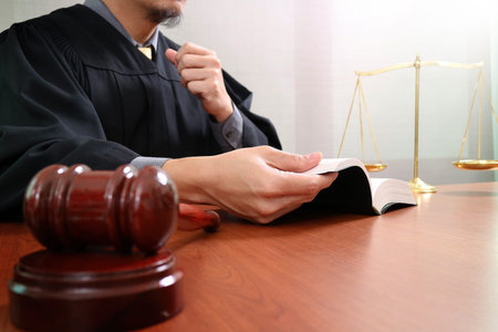 justice and law concept.Male judge in a courtroom with the gavel,opening holy book and digital tablet computer with brass scale on wood tableの写真素材