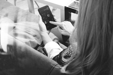 brunette woman using smart phone and digital tablet computer on sofa in living room,black and whiteの写真素材