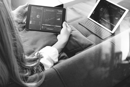 brunette woman using digital talet and laptop computer on sofa in living room,black and whiteの写真素材
