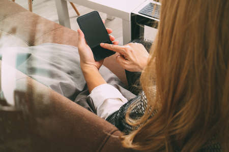 brunette woman using smart phone and digital tablet computer on sofa in living roomの写真素材