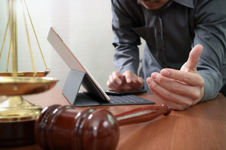 justice and law concept.Male lawyer in office with the gavel,working with smart phone and digital tablet computer and brass scale on wood tableの写真素材