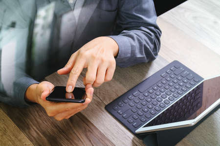 top view of businessman hand using smart phone,mobile payments online shopping,omni channel,digital tablet docking keyboard computer in modern office on wooden desk,filterの写真素材